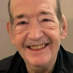 Smiling older gentleman wearing a dark jacket.
