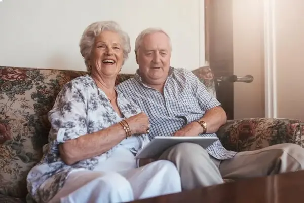 Smiling elderly couple sitting together on a sofa at home, enjoying independent living in later life.