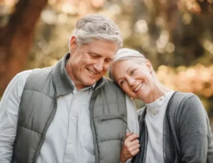 Smiling senior couple outdoors leaning on each other, symbolising support and comfort in later life.