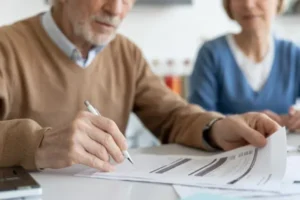 Older man reviewing financial documents at home with his partner, checking benefits and support options.